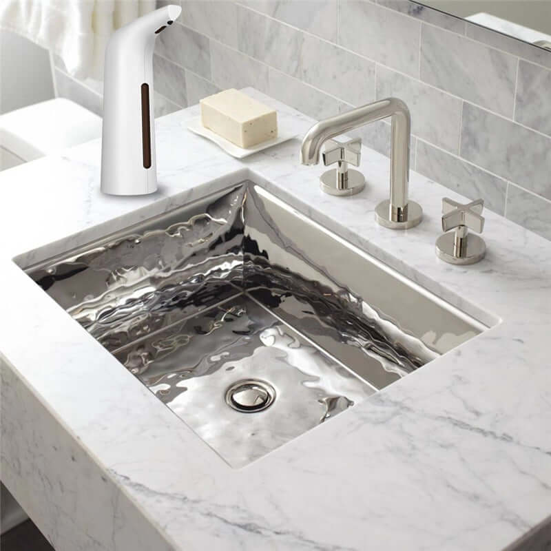 Touchless automatic induction liquid dispenser next to a modern marble sink with soap bar and faucet.